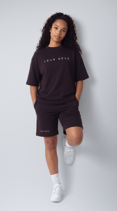 Woman wearing the Leur Rêve Short in black, one knee raised, wordmark at the hem