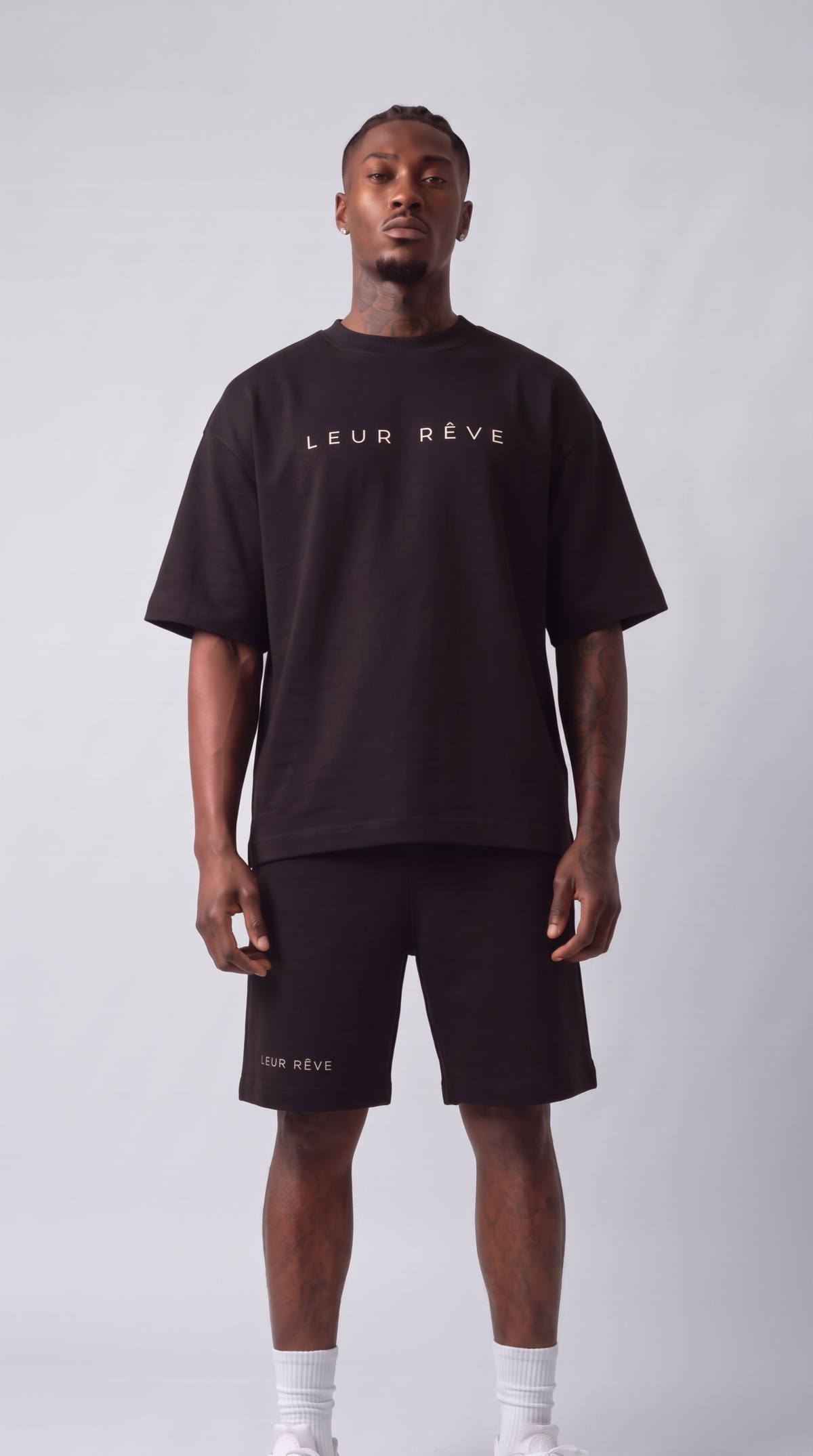 Man wearing the Leur Rêve Tee in black with the matching short, standing, front view
