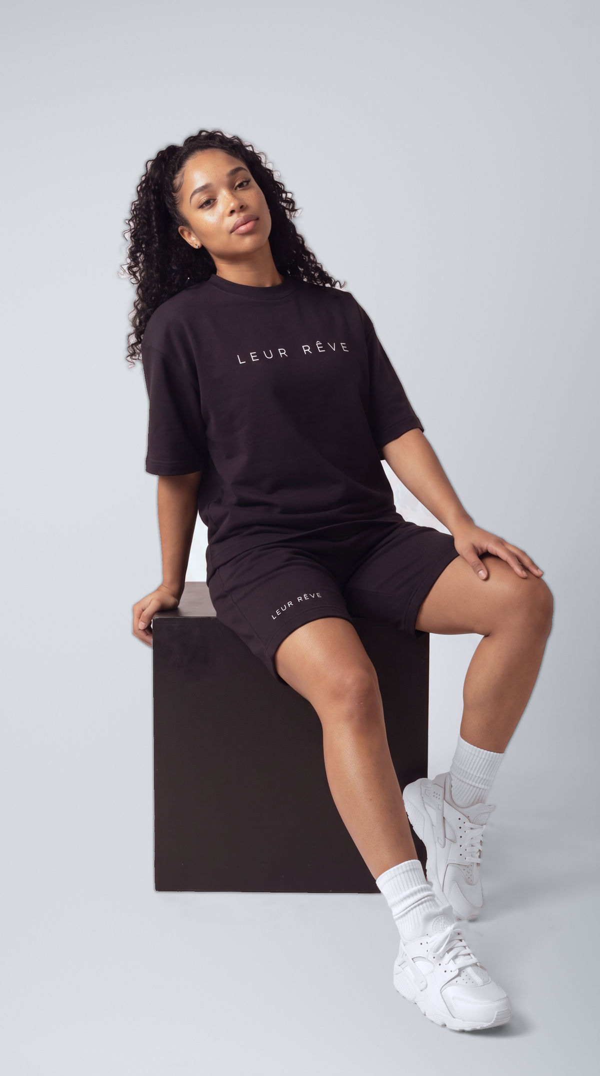 Woman wearing the Leur Rêve Set in black, seated on a block