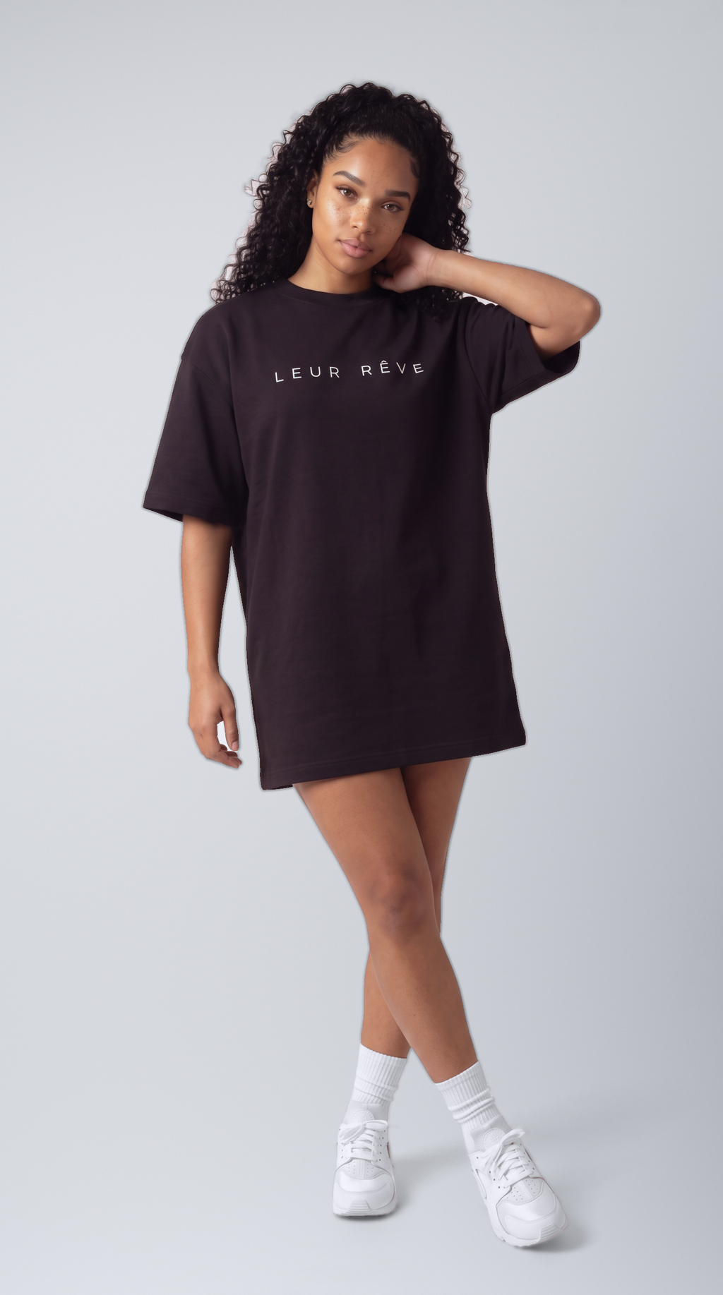 Woman wearing the Leur Rêve Tee in black, hand at neck